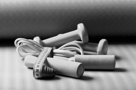 Skipping rope, dumbbells in cyan color tied with measuring tape on green and purple background. Sports and health idea. Workout and refreshment concept. Tape around jump rope and barbells on yoga mat.の写真素材