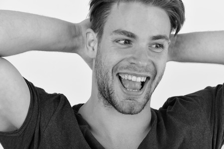 Man with fair hair on white background. Macho with cheerful face holds hands behind head, close up. Guy with bristle in dark blue tshirt smiles widely. Confidence and emotions concept.の写真素材