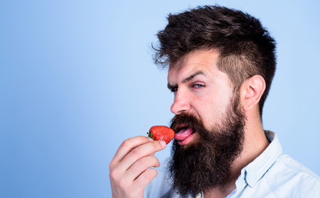 Erotic concept. Oral pleasure. That is how tastes summer. Man handsome sexy hipster with long beard licking strawberry tongue. Hipster enjoy juicy ripe red strawberry. Man licking sweet berry.の写真素材