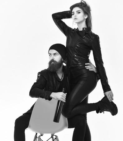 Couple in love with curious faces on white background. Rock lovers drink spirits. Street life style concept. Girl and bearded man in black leather jacket lean on orange chair holding bottle of alcohol.の写真素材