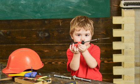 Toddler on busy face plays with screwdriver tool at home in workshop. Kid boy play as handyman....