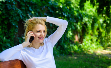Pleasant conversation. Girl blonde smiling face talk smartphone green nature background. Woman having pleasant conversation in park. Girl modern smartphone calling friend cell phone.の写真素材