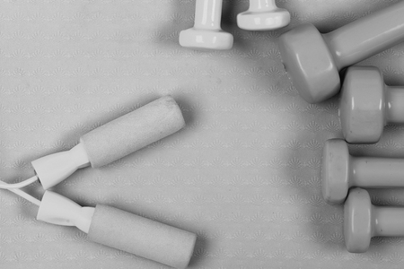 Sports and healthy lifestyle concept. Barbells in pink, green and blue colors near skipping rope, top view. Dumbbells and jump rope on purple texture background. Shaping and fitness equipment.の写真素材