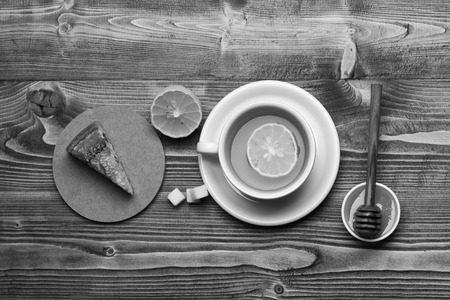 Tea cup with honey and piece of cake making cozy composition, top view. English tea time concept. Cup of green tea with slice of orange fruit. Hot beverage with sugar cubes on wooden background.の写真素材