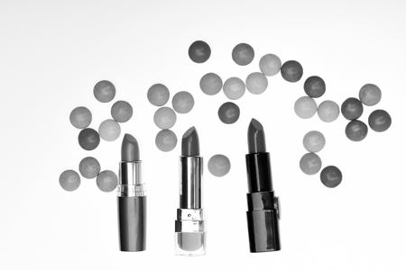 Red or scarlet lipsticks near colorful dragee sweets. Quality of cosmetic supplies, smell, color, taste. Lipsticks isolated on white background, top view. Smell and taste of lipstick concept.の写真素材