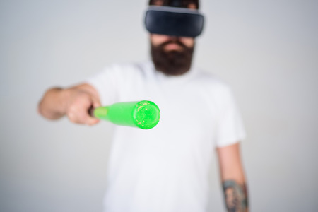 Man with beard in VR glasses holds baseball bat, grey background. VR sportsman concept. Guy with VR glasses play baseball. Hipster on concentrated face pointing forward with bat, selective focus.の写真素材