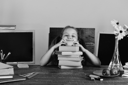 Schoolgirl with happy and funny face expression lies on pile of books. Kid and school supplies on...