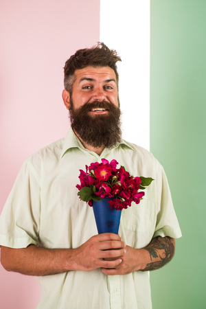 Flowers delivery concept. Man with beard cheerful face holds bouquet fresh flowers. Guy holds bouquet confident about date. Delivery man with flowers. Hipster with beard ready holiday congratulate.の写真素材