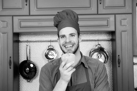 Guy in chef hat smile with yellow pepper in kitchenの写真素材