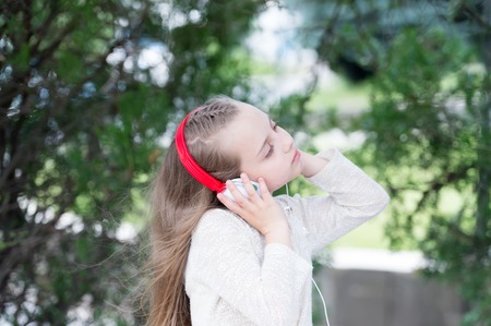 Little girl listen music in summer park. Melody sound and mp3. Child enjoy music in headphones outdoor. Fashion kid and modern technology. Summer vacation and funの写真素材