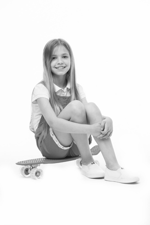Small girl sit on skate board isolated on white. Child skater smile with longboard. Skateboard kid in pink jumpsuit. Sport activity and energy. Childhood and active games. Beauty on skateboard.の写真素材