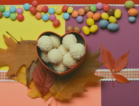 Coconut candy in a red heart on colorful background. Sweets near autumn leaves, colorful sweets,...