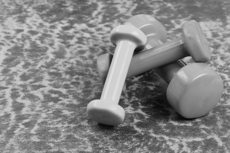 Dumbbells made of plastic on burgundy texture background. Shaping and fitness equipment. Healthy shape and sport concept. Barbells in green, pink and cyan color placed on wooden surface, close upの写真素材
