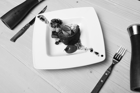 French meal and cooking concept. Baked pork steak laid in circle on salad on yellow wooden background. Dish with modern presentation on square plate. Table served for one in restaurant or cafe.の写真素材