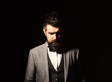 Business and style concept. Businessman with serious face isolated on black background. Man with long beard and bow tie. Macho in formal suit has stylish haircut.の写真素材