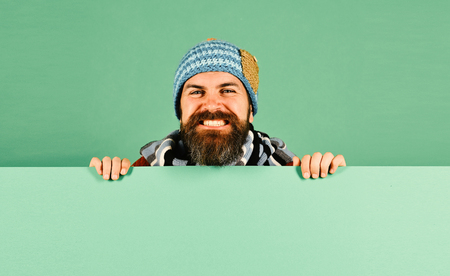 Autumn and demi season clothes concept. Hipster with beard and wide smile wears warm clothes. Man in warm hat on green background, copy space. October and November sale ideaの写真素材