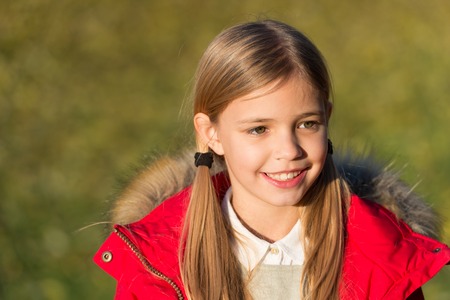 Child blonde long hair walking fall park background. Feel happy sunny autumn day. Girl happy wear coat with hood enjoy fall nature. Child wear coat for fall season. Fall clothes and fashion concept.の写真素材