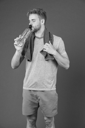 Man drink water after training on violet background. Thirsty sportsman with plastic bottle on purple background. Thirst and dehydration. Drinking water for health. Sport activity and energy.の写真素材