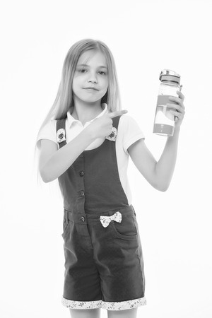 Girl on smiling face posing with bottle of water, isolated on white background. Kid girl with long hair pointing at bottle with water. Water balance concept. Girl cares about health and water balance.の写真素材