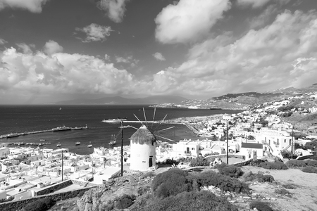 Seascape from Mykonos, Greece. Village windmill on mountain landscape by blue sea. White houses on cloudy sky with nice architecture. Wanderlust and travel. Summer vacation on mediterranean island.の写真素材