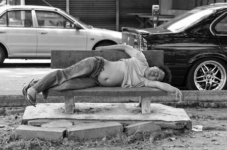 Kuala Lumpur, Malaysia-April 4, 2007: Homeless man sleep on bench on urban background. Beggar on street. Living on streets. Poverty. Helping those less fortunate.のeditorial素材
