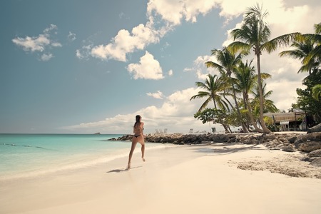 Young pretty woman with beautiful body in swimsuit running in ocean water sunny day at tropical beach, wellness conceptの写真素材