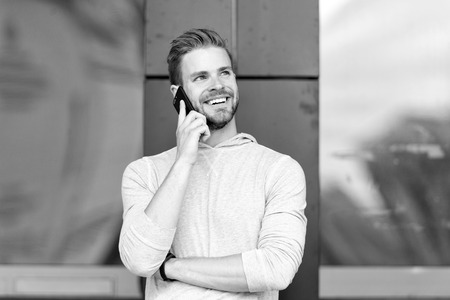 Happy to hear you. Man bearded walks with smartphone, urban background. Man pleasant smiling face...