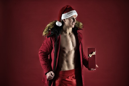 Gift delivery service. Handsome santa concept. Athlete man wear santa hat. Macho muscular torso posing with gift box. Santa claus gift courier. Sexy athletic macho muscular chest in santa claus hat.の写真素材