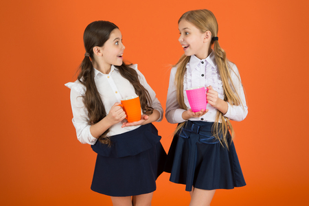 Tea break. Girls kids school uniform orange background. Schoolgirl hold mug. School lunch. Having break relax. Drinking tea while break. School mates relaxing with drink. Hydration and water regime.の写真素材