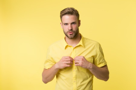 It is hot here. I will show you my sexy body. Man handsome bearded guy undressing yellow background. Guy confident attractive macho feels sexy while unbuttoning shirt. Want to see sexy torso.の写真素材