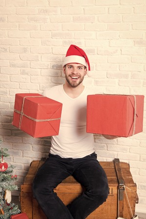 Holidays preparation and celebration. Man santa smile with boxes on white brick wall. Happy boxing day. Gift giving and exchange concept. Macho in christmas hat hold wrapped presents.の写真素材
