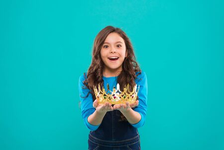 My biggest treasure. Kid hold golden crown symbol of princess. Childhood concept. Every girl dreaming to become princess. Lady little princess. Girl cute baby hold crown while stand blue background.の写真素材
