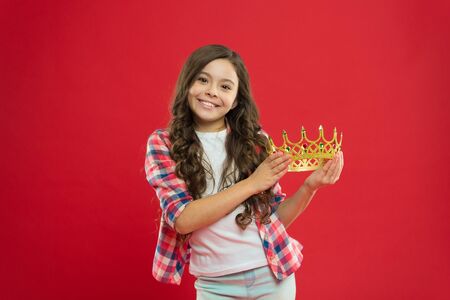 My biggest treasure. Kid hold golden crown symbol of princess. Childhood concept. Every girl dreaming to become princess. Girl cute baby hold crown while stand red background. Lady little princess.の写真素材