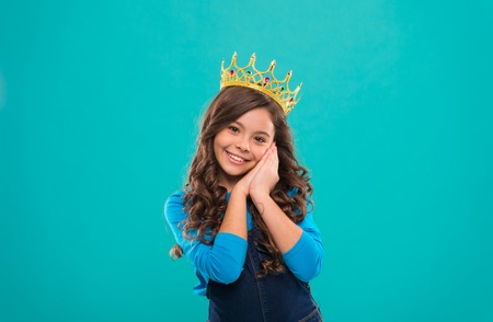 Beauty contest model. Kid wear golden crown symbol of princess. Girl cute baby wear crown while stand blue background. Childhood concept. Every girl dreaming to become princess. Lady little princess.の写真素材