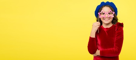 Birthday party photo booth props. Kid girl cheerful posing with eyeglasses party attribute. Lets have fun. Party accessories concept. She ready start party. Child with long hair and fashionable hat.の写真素材