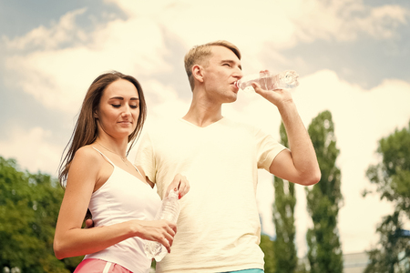 Sport and health. Summer activity and energy. Couple of coach relax after workout. Girl and guy sunny outdoor. Woman and man drink water from bottle.の写真素材