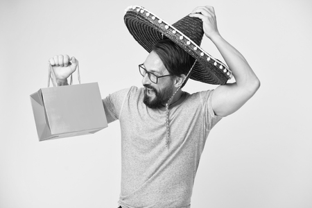 Man cheerful face sombrero hat holds shopping bag yellow background. Guy with beard festive in sombrero. Man festive mood holds shopping bag. Seasonal sale and discount. Holiday and gift concept.の写真素材