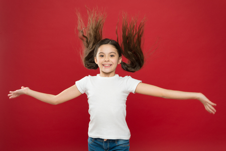 Kid smiling cute face live carefree happy life. Enjoy every moment. Young and free. Happy child girl with long hair on red background. Happiness and joy. Positive emotions. Child care and upbringing.の写真素材