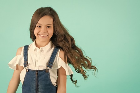 Child smiling with healthy brunette hair. Girl smile with flowing long wavy hair on blue background. Kid beauty salon concept. Haircare, hairstyle, hairdresser, barber, punchy pastel, copy spaceの写真素材