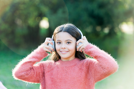 Keeping her connected to her entertainment. Adorable little girl outdoor. All she wants to hear is music. Little girl child wearing headphones. Happy child enjoy listening to music on the go.の写真素材