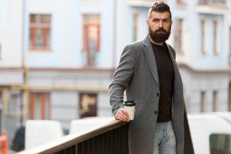 Man bearded hipster drink coffee paper cup. One more sip of coffee. City lifestyle. Businessman well groomed appearance enjoy coffee break out of business center urban background. Relax and recharge.の写真素材