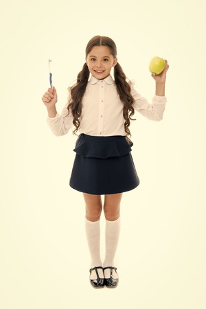 Healthy habits. Girl cute holds toothbrush and apple white background. Brush teeth concept. Child girl smiling face holds apple and toothbrush. Child school girl smart kid happy face cares hygiene.の写真素材