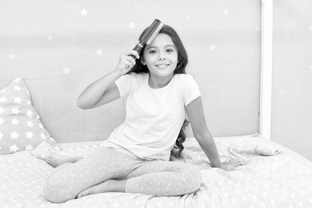 Beauty salon tips. Girl long curly hair grey interior background. Child curly hairstyle hold hairbrush or comb. Apply oil before combing hair. Healthy hair. Conditioner or mask organic oil comb hair.の写真素材