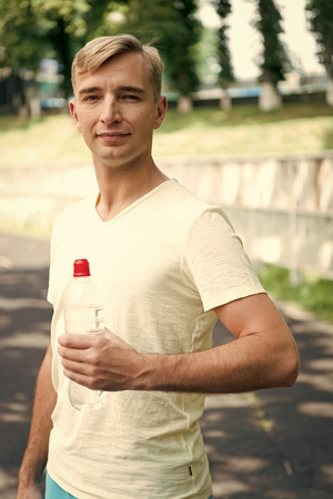 Thirsty man with water bottle on stadium. Sportsman with plastic bottle on sunny outdoor. Thirst and dehydration. Drinking water for health. Sport activity and energy.の写真素材