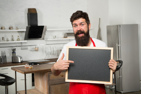 Be our guest. Restaurant or cafe menu. Advertisement. Man chef with board, copy space. Mature male. Bearded man cook. Hipster in kitchen. Bearded man in red apron. Ready to order. Food concept.の写真素材