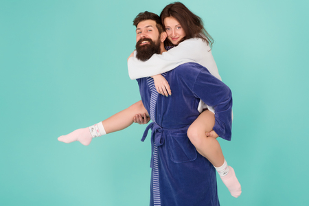 Lets stay at home and have fun. Couple in bathrobes having fun turquoise background. They always have fun together. Close relationship. Handsome young man giving his girlfriend piggyback ride.の写真素材