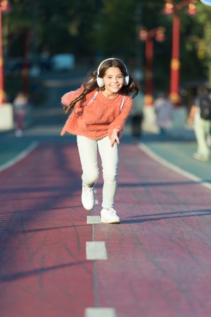 Playlist for active day. Girl cute with headphones. Little child enjoy activity. Kid walking running in park listening music. Music fills me with energy. Enjoy walk with favorite music in headphones.の写真素材