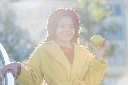She likes apple best of all fruits. French fashion. Happy little girl holding juicy green apple. child with apple fruit on sunny day. Cheerful kid enjoy apple crop in autumn. Healthy snack for a kid.の写真素材
