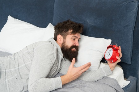 Too early. bearded man hate alarm clock while lying in bed at home. man with alarm clock. morning wake up. Man sleep on bed. Time to take break. Depressed man. Late again. Feeling tired and stressed.の写真素材