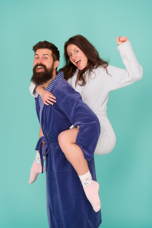 Couple in bathrobes having fun turquoise background. Lets stay at home and have fun. They always have fun together. Enjoying every second together. Handsome young man piggybacking beautiful woman.の写真素材